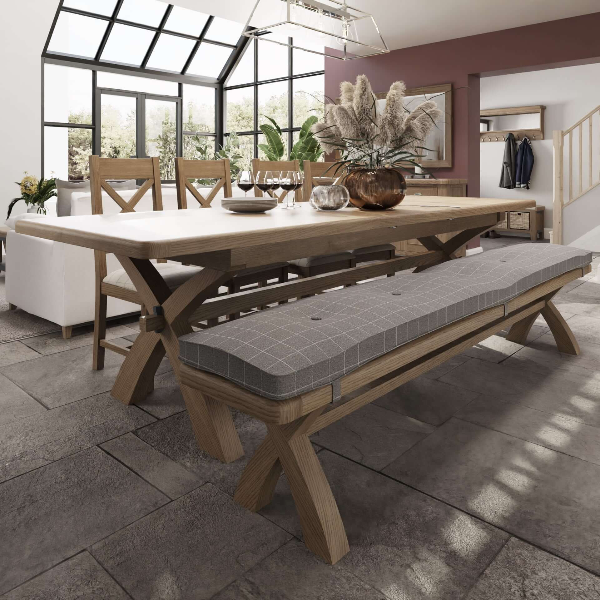 2.5-3.0m oak trestle extending dining table in an extended position in life setting. Table set with 8 seats (4 dining chairs and 4 seats on a bench with cushion). The table has space for additional 2 seats on each side when extended. Table is decorated with vase with dry flowers and cutlery. 