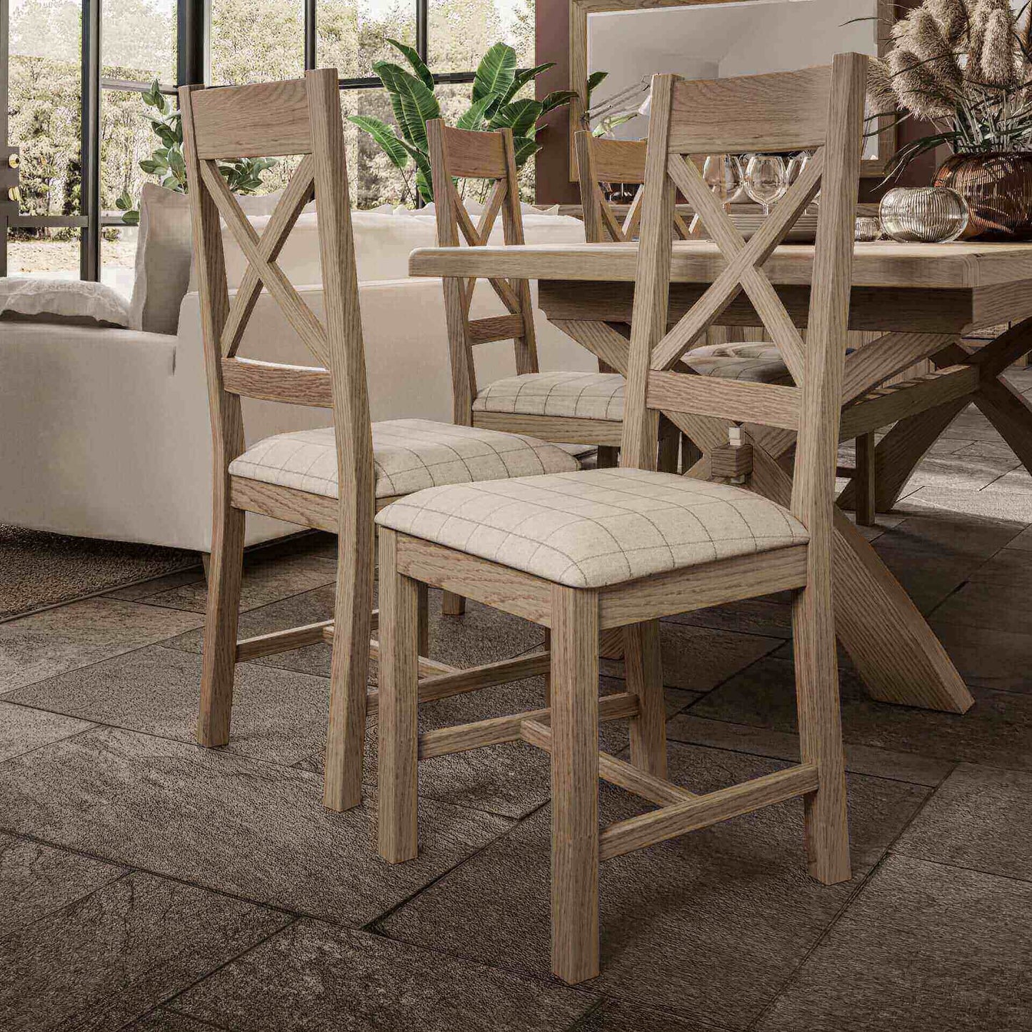 Set of two oak cross back dining chair with beige wool upholstered padded seat shown from both front and back next to a cross leg table.