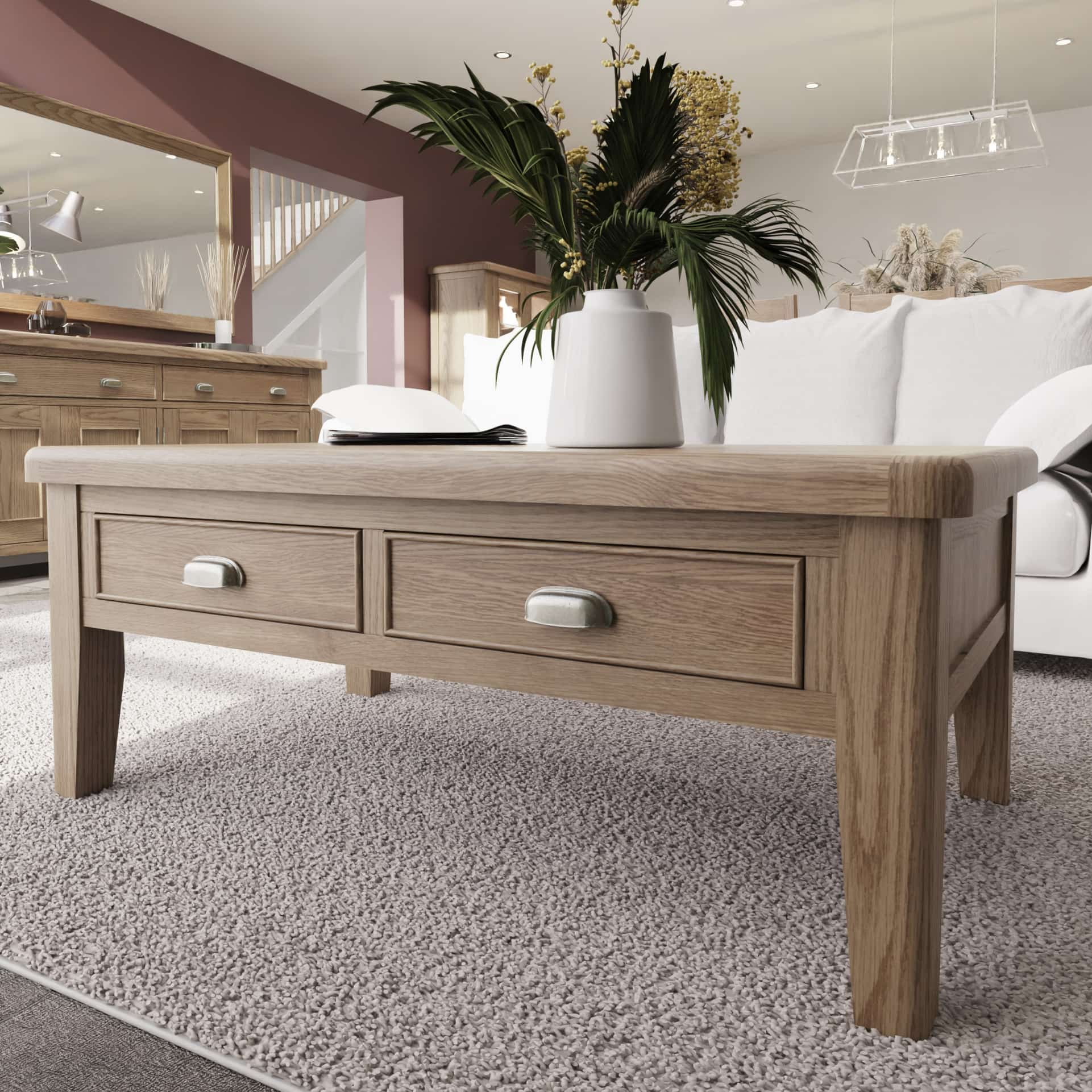 Large oak coffee table with 4 drawers is shown in a room setting. Standing on a carpet next to a sofa with flowers and journals on top