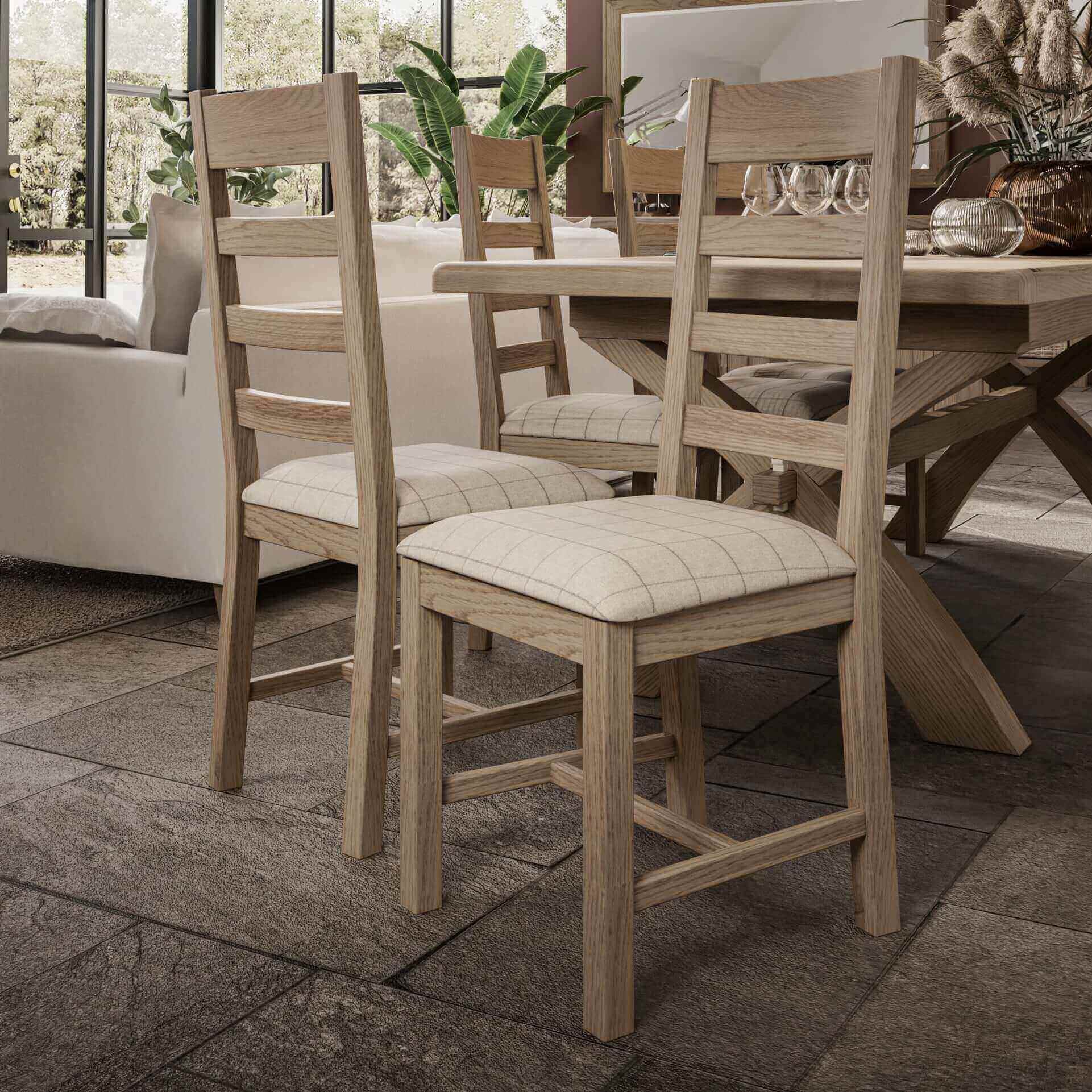 Set of 2 oak slat back dining chairs with padded beige wool seats pictured from both sides next to the dining table