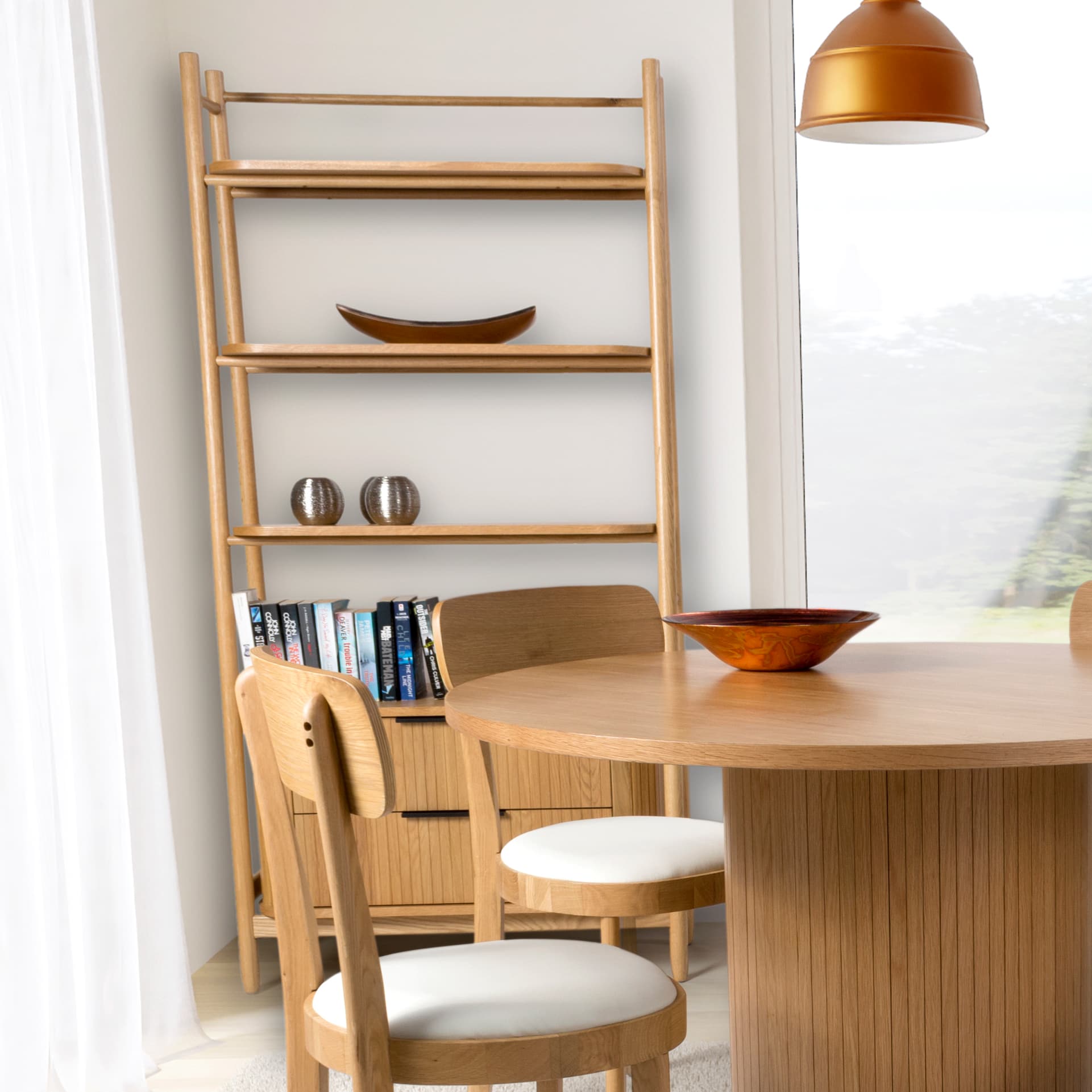 Tall oak bookcase shown in room setting behind the dining table with books and decor