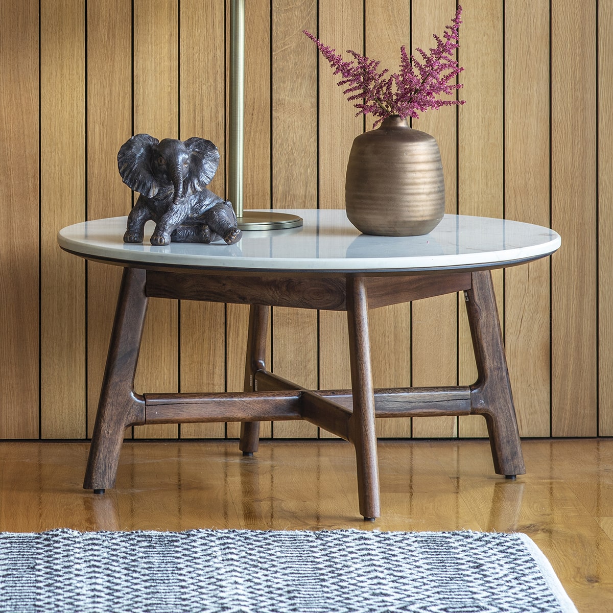 Close side look at wood and marble round coffee table and its leg structure with decor of statuette and a vase with flowers