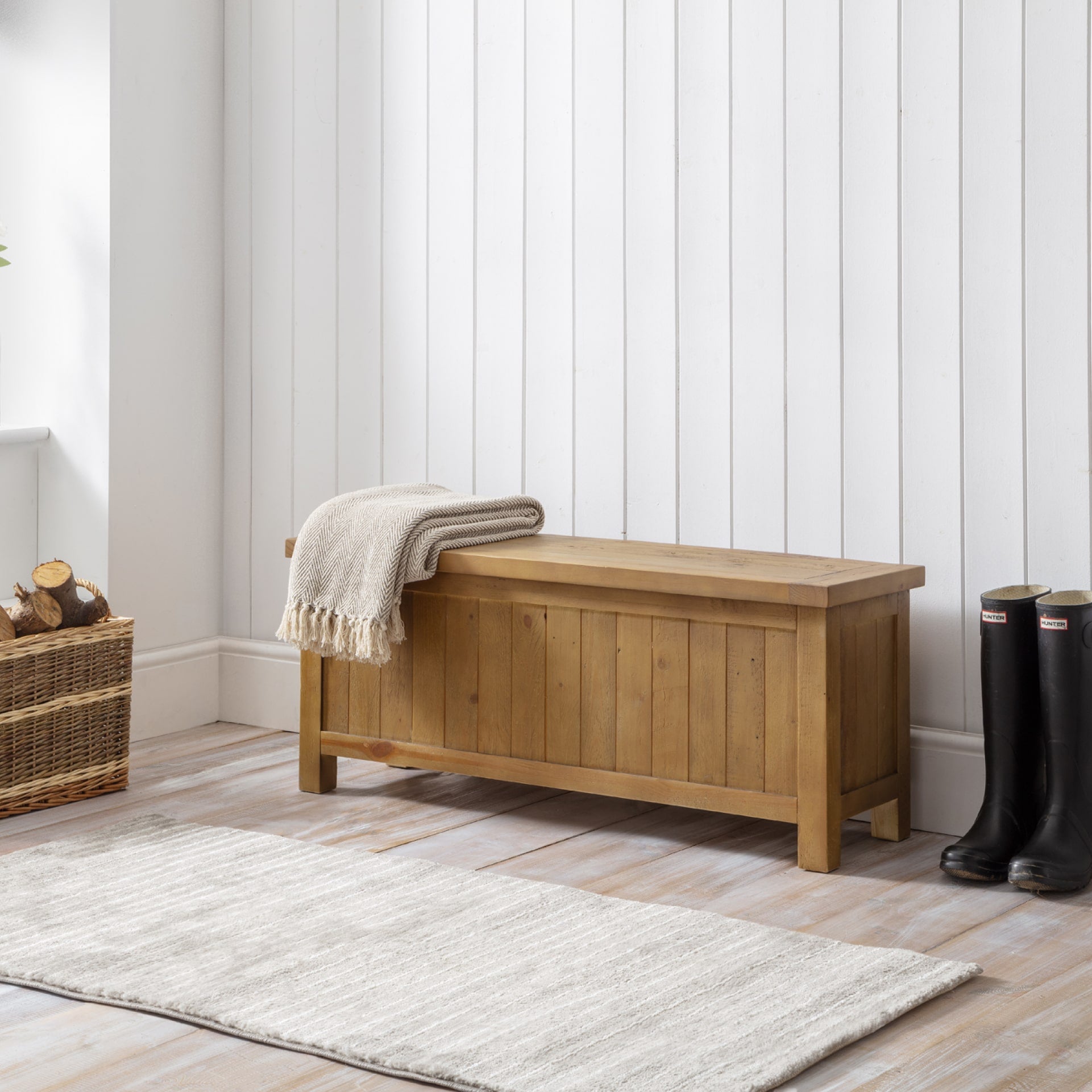 Pine storage bench is shown in a mudroom interior with fire wood, blanket and wellies