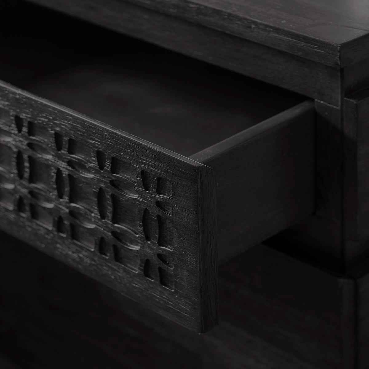 Close-up view on the partly open top drawer of the two drawer wooden black nightstand. The blind fretwork on the top drawer can also be seen clearly. 