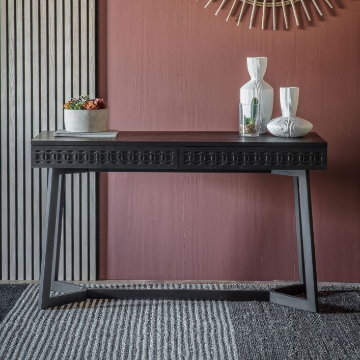 Black wooden desk with 2 drawers and geometric leg structure in a room setting with decor used as a console table