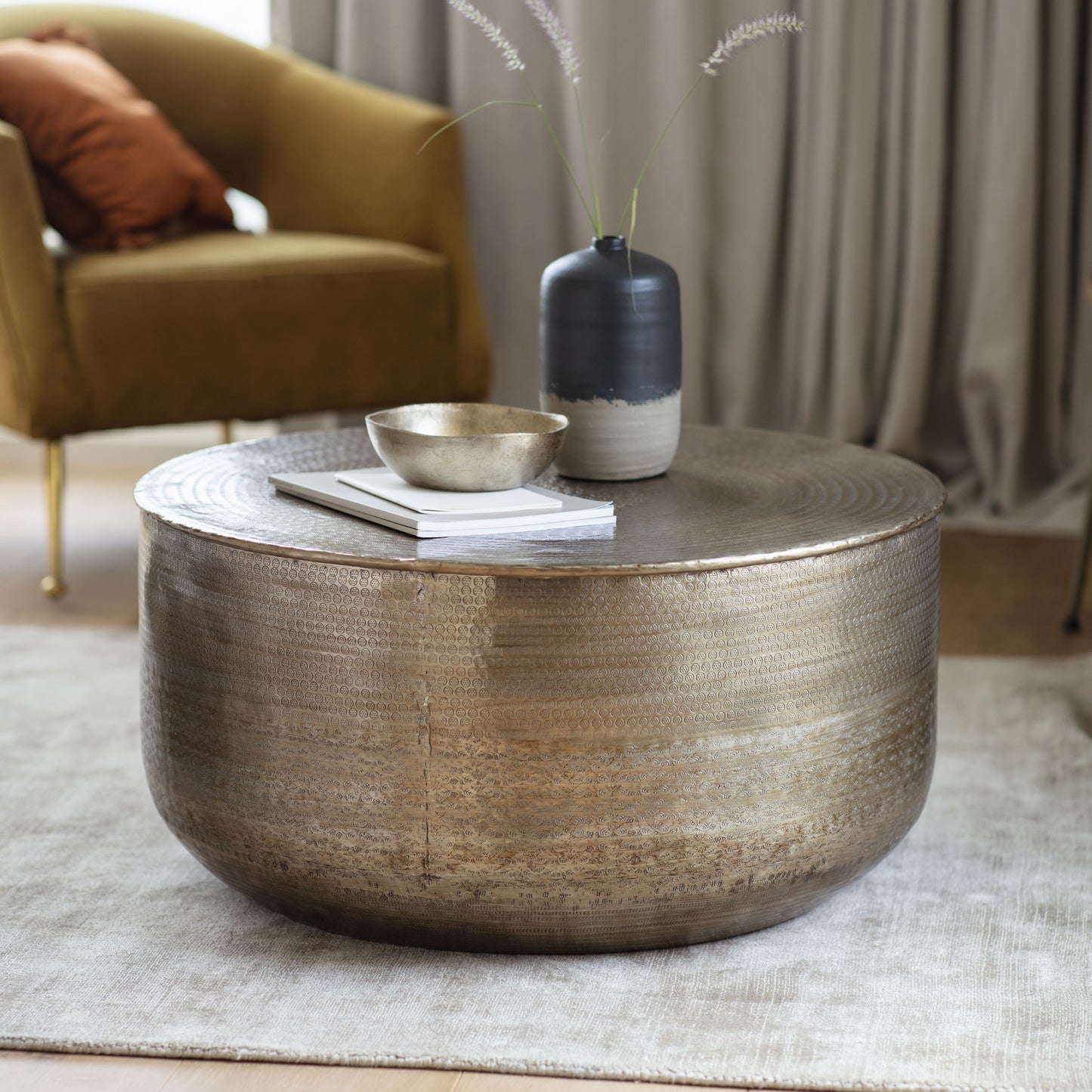 Brass coloured hand pressed metal coffee table in the room setting with flower vase